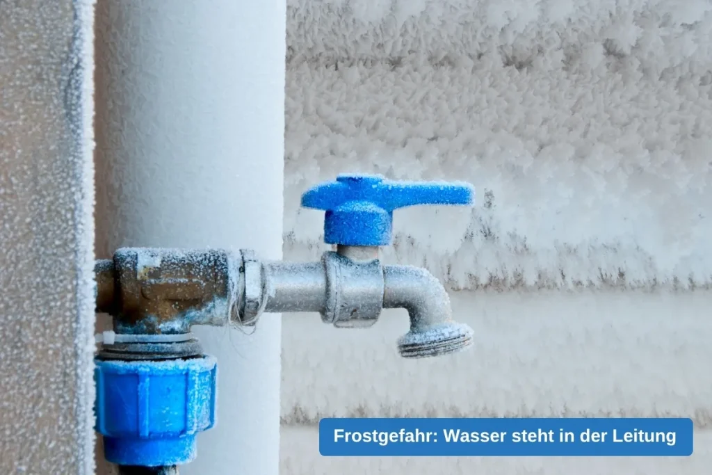 Wasserhahn mit blauem Griff an einer frei liegenden Leitung, Armatur und Wand mit Raureif überzogen
